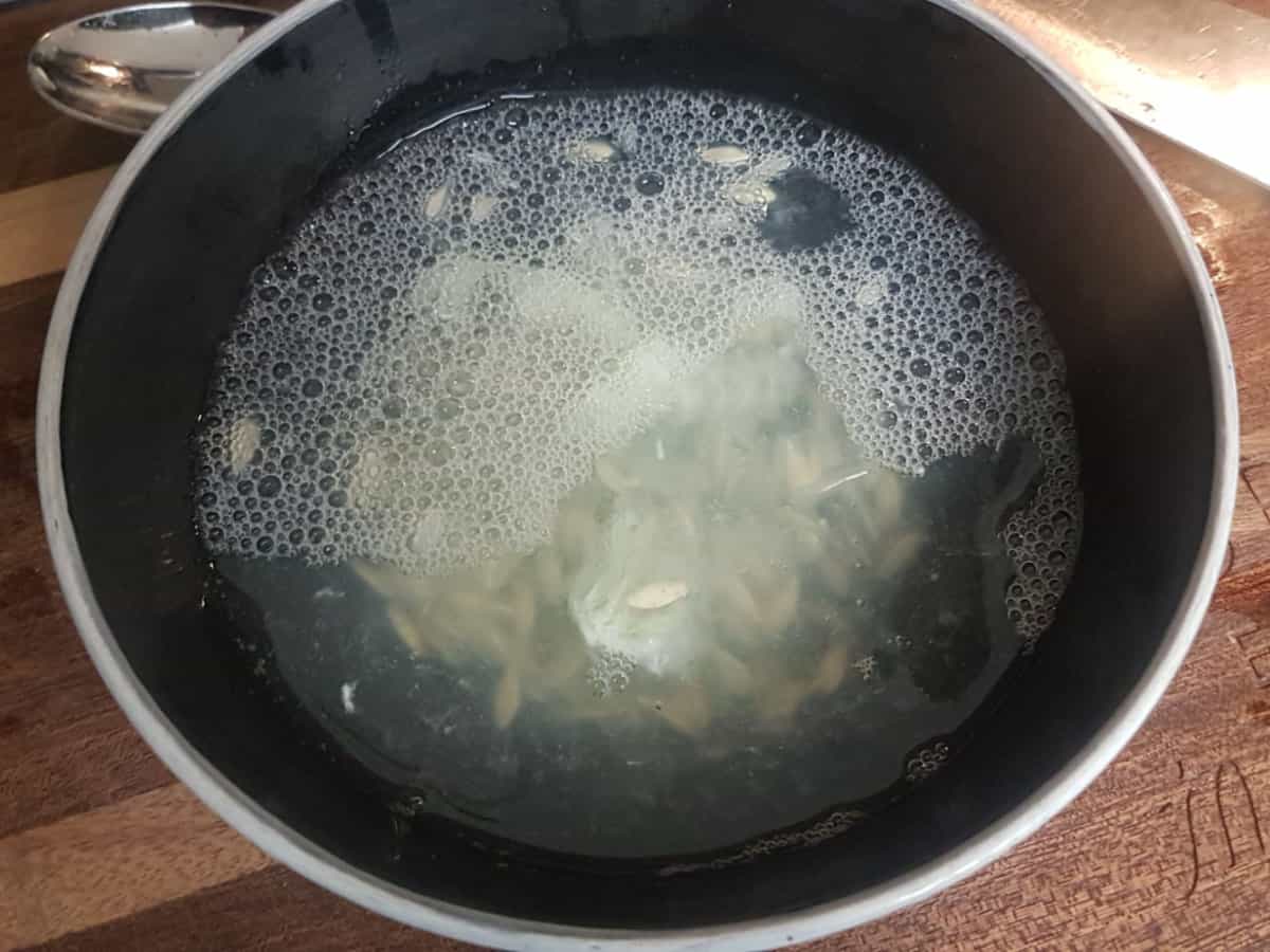 A black bowl filled with fresh cucumber seeds and water to ferment. The bowl is on a wooden cutting board.