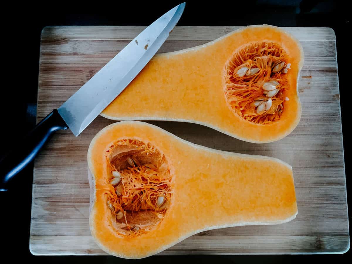 A butternut squash cut in half and displayed on a grey wood cutting board.