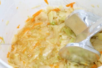 Shredded carrot and cabbage in a salt brine in a white bucket.