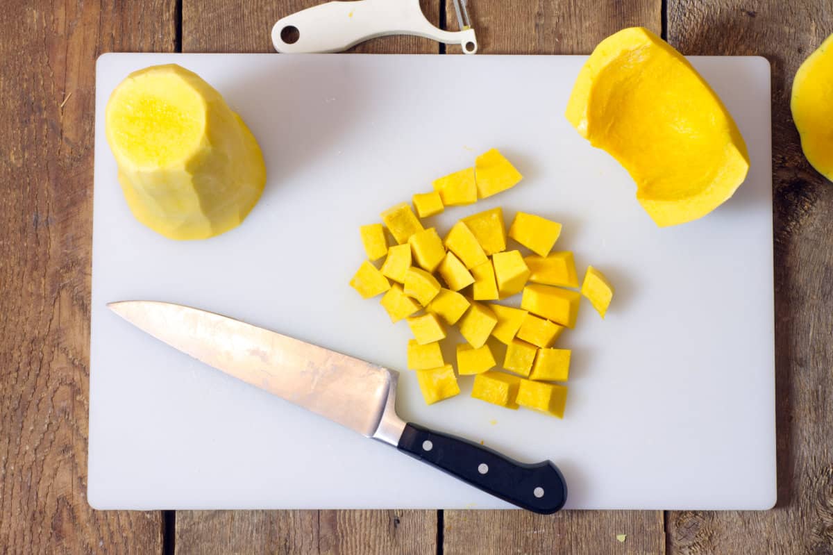 a top down view of a peeled butternut squash cut into various shapes on a white cutting board.