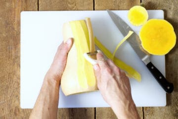 A overhead view of a butternut squash being peeled with a vegetable peeler.