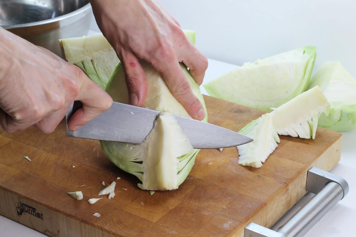 A quarter section of green cabbage having its core cut out on a wooden cutting board.