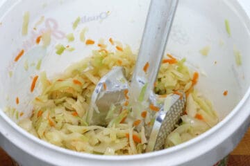 Pounding shredded cabbage and carrot in a bucket to extract brine when making sauerkraut.