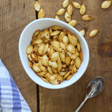 Over head image of air fryer roasted pumpkin seeds in a round white porcelain bowl on a barn board background.