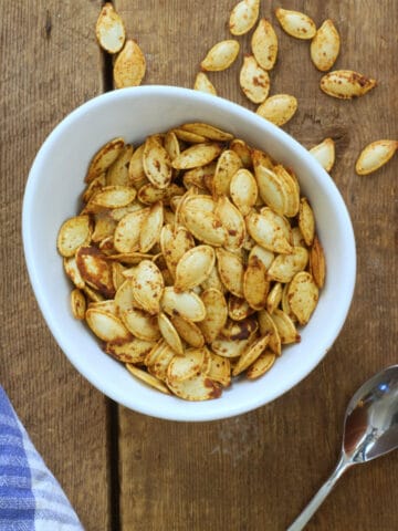 Over head image of air fryer roasted pumpkin seeds in a round white porcelain bowl on a barn board background.