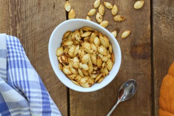 Over head image of air fryer roasted pumpkin seeds in a round white porcelain bowl on a barn board background.