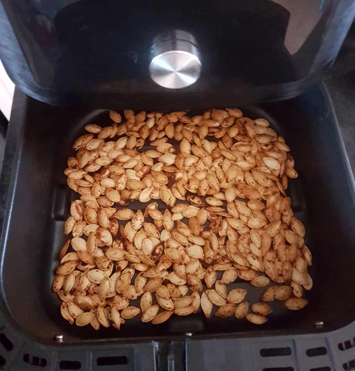 Golden brown roasted pumpkin seeds in an air fryer basket.