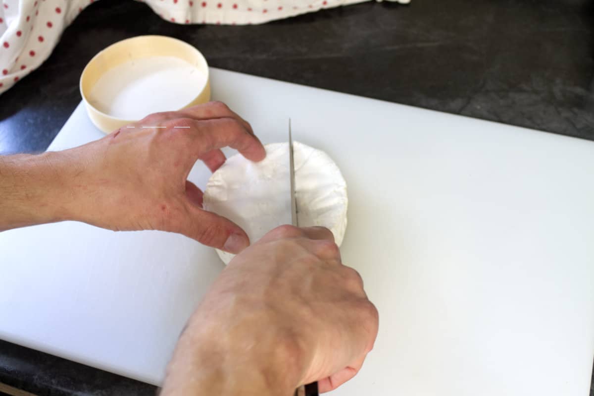 A wheel of brie on a white cutting board being about to be cut.