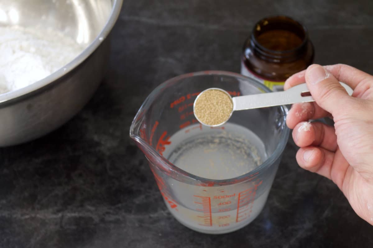 Active dry yeast in a teaspoon measure being added to a measuring cup of water.