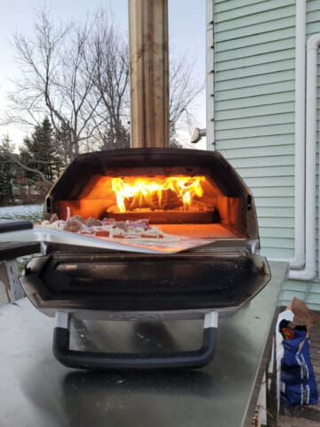 Firing an ucooked meatball pizza into a lit Ooni Karu pizza oven with a stainless steel pizza peel.