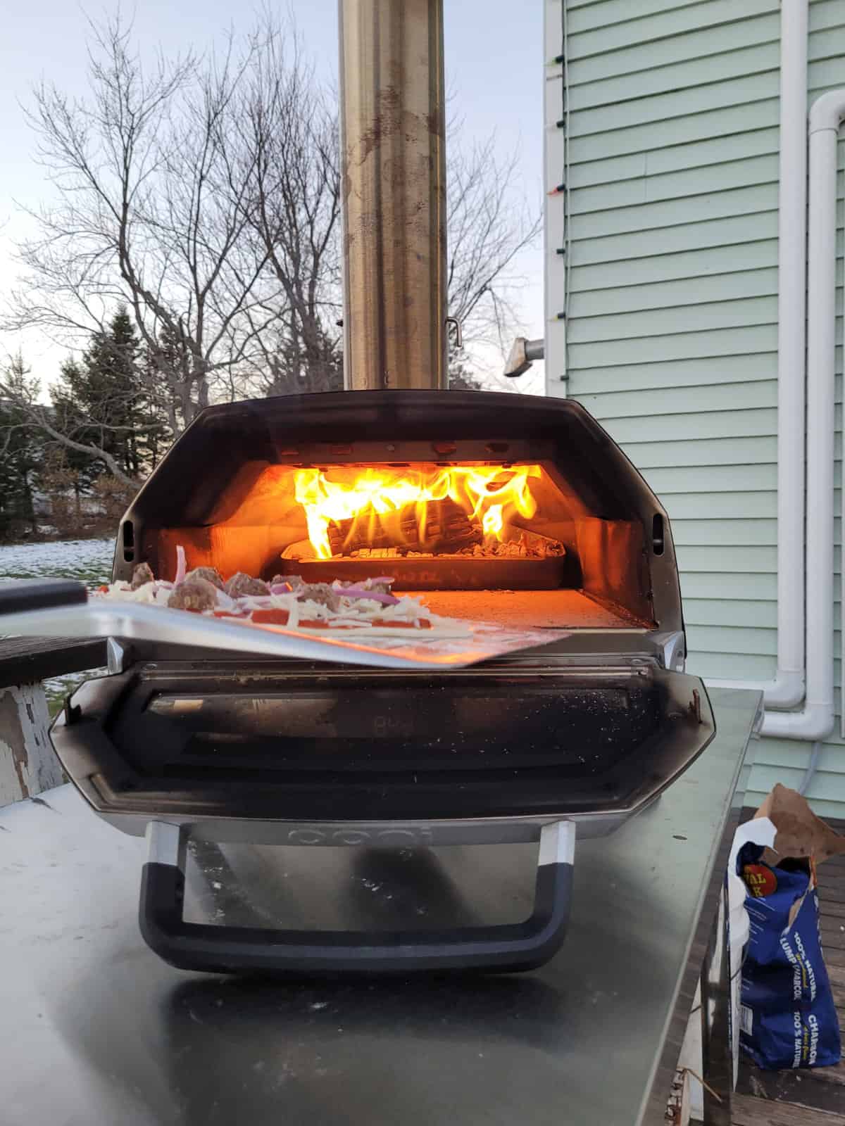 Firing an ucooked meatball pizza into a lit Ooni Karu pizza oven with a stainless steel pizza peel.