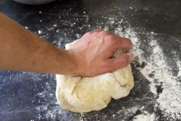 A ball of dough being kneaded on a counter top.