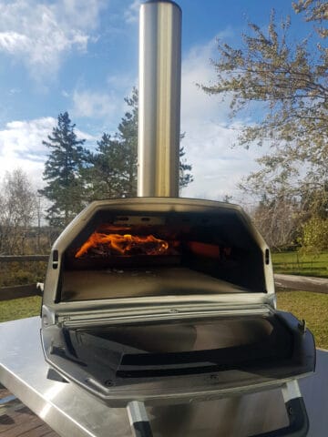 An Ooni Karu 16 pizza oven with the door open and fire visible in the background.