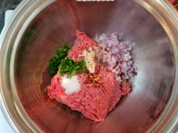 All the ingredients for meatballs in a stainless steel bowl.