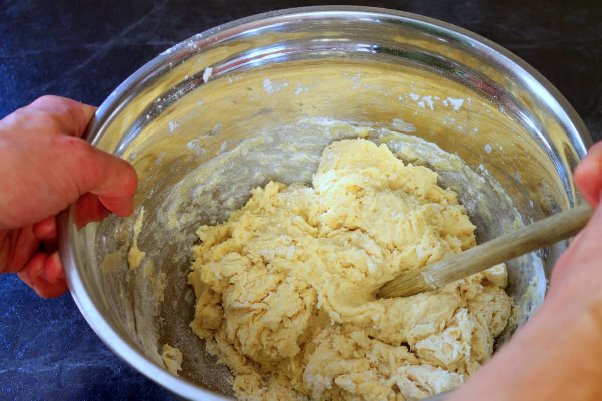 Mixing the pull apart bread ingredients in a stainless steel bowl with a wooden spoon.