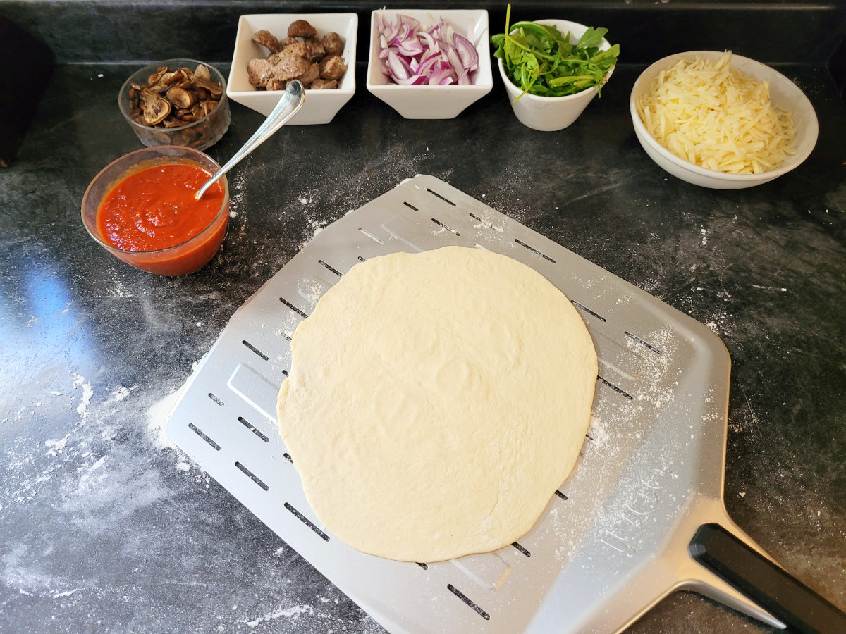 All the ingredients and toppings needed to assembal and cook a meatball pizza layed out on a black counter top.