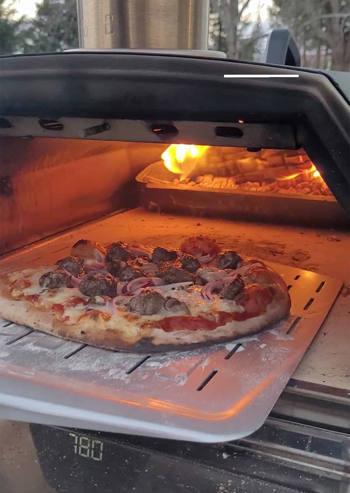 Taking out a meatball pizza from the Ooni pizza oven.