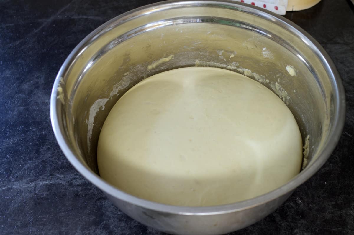 A stainless steel bowl filled with a large puffy, and fully proofed ball of dough.