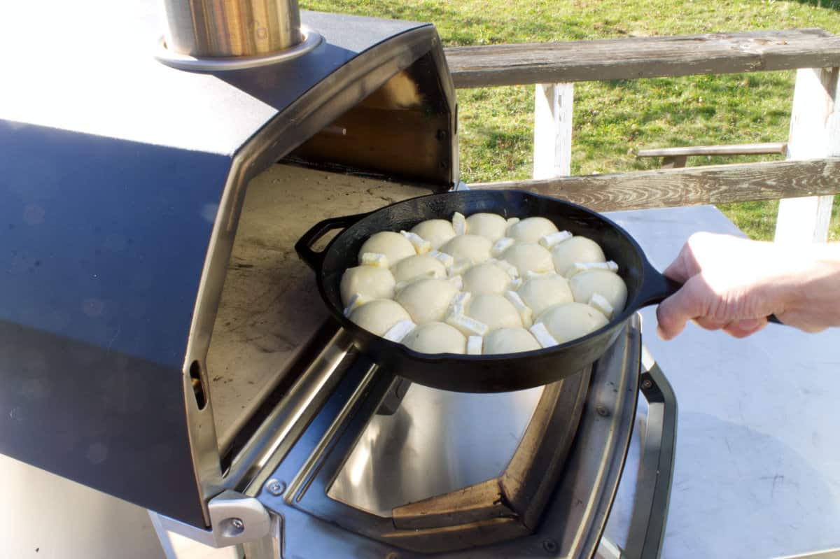 A cast iron skillet of cranberry pull apart bread going into the ooni karu pizza oven.