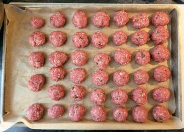 Overhead shot of formed, raw meatballs on a sheet pan before baking.