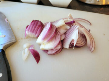 A close up shot of sliced red onion on a white cutting board.
