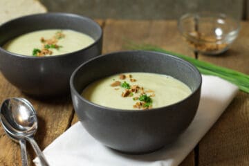 Horizontal closeup image of broccoli and cauliflower soup served in black stoneware bowls and garnished with chopped chives and chopped almonds.