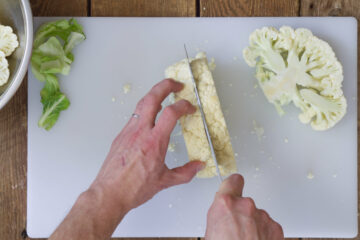 Top down view of cauliflower being cut into thick steak like slices.