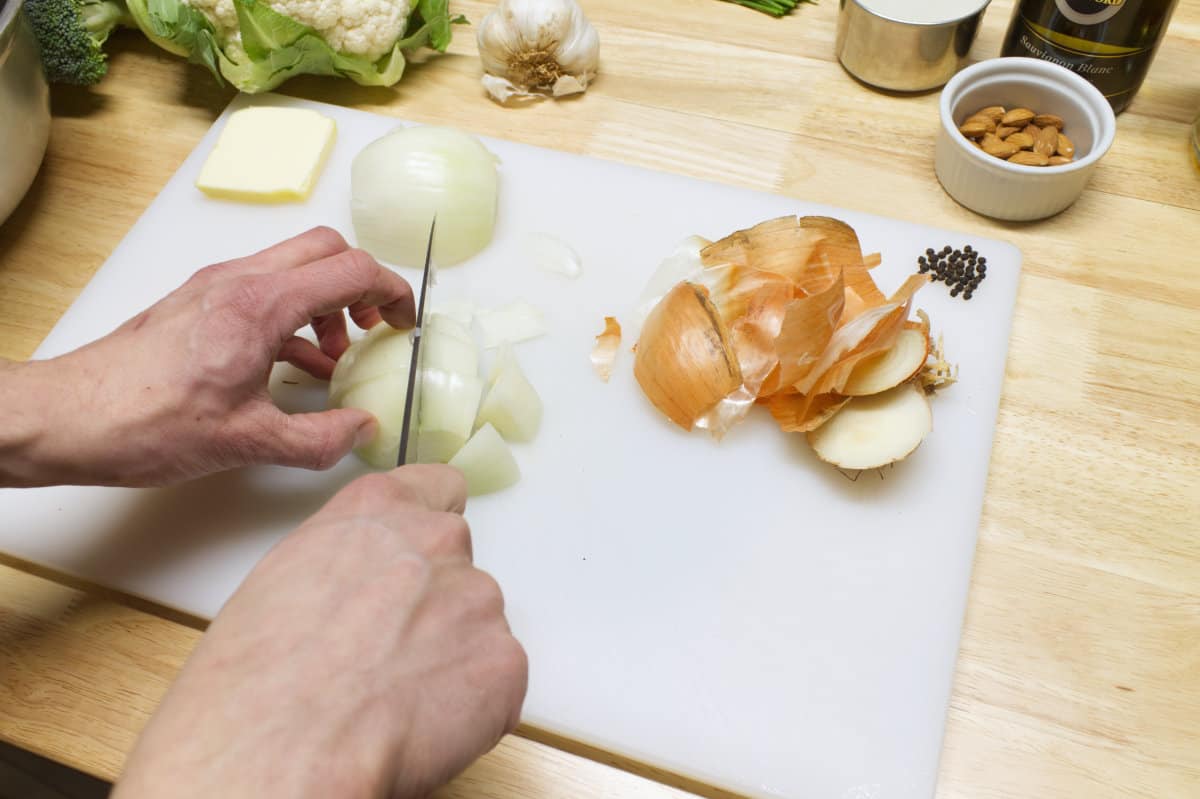 Spanish onion being chopped on a white cutting board, and surrounded by other ingredients.
