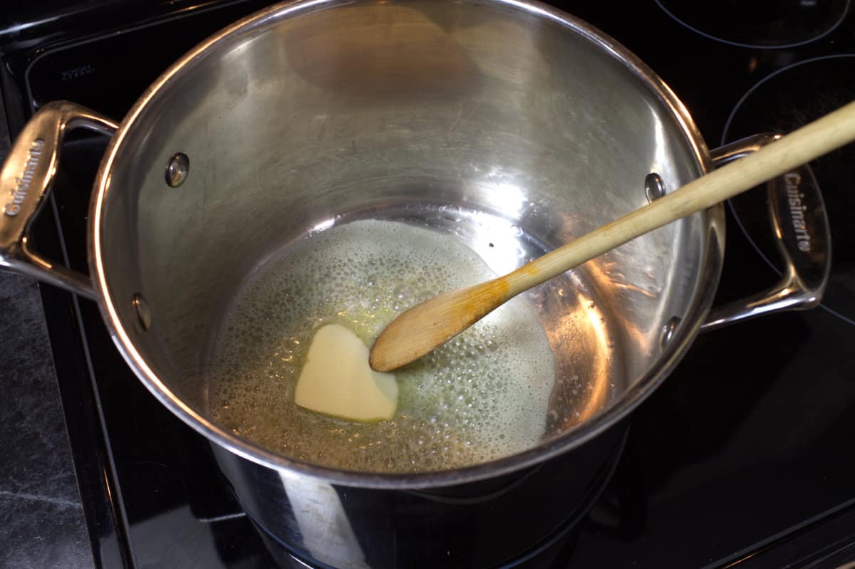 Melting butter in a large stainless steel soup pot with a wooden spoon.