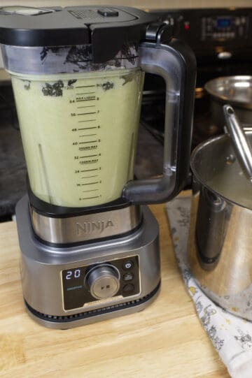 A ninja foodie stand blender on a wood block countertop and filled with broccoli and cauliflower soup after blending.