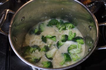 overhead shot of broccoli and cauliflower simmering in a milky liquid in a soup pot.