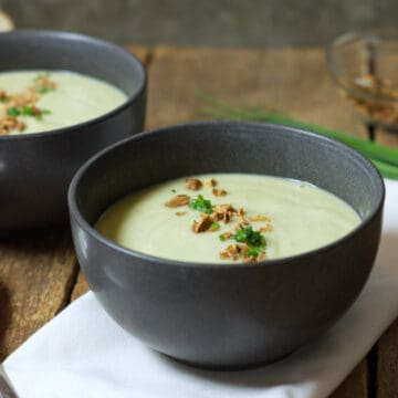 Square closeup image of broccoli and cauliflower soup served in black stoneware bowls and garnished with chopped chives and chopped almonds.