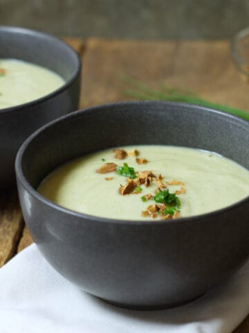 Square closeup image of broccoli and cauliflower soup served in black stoneware bowls and garnished with chopped chives and chopped almonds.