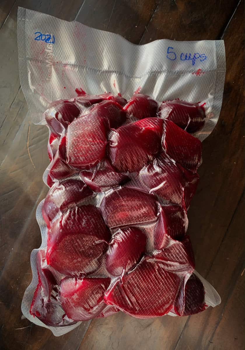 Blanched and peeled beets vacuum sealed in a small bag and displayed on a wooden counter.