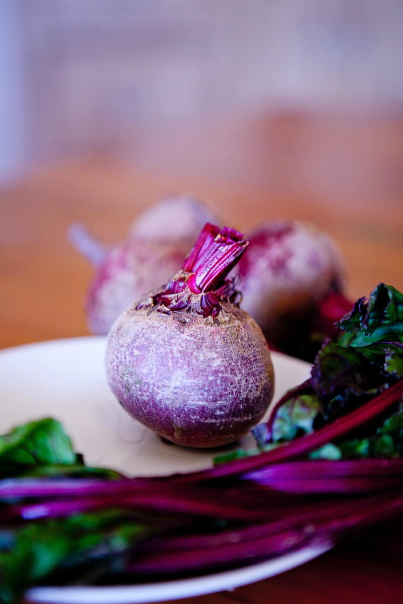 A vertical image of a red beet on a cutting board with its leaves trimmed off.