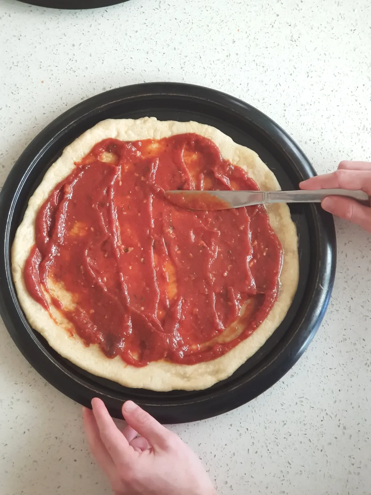 Spreading pizza sauce on homemade pizza dough base