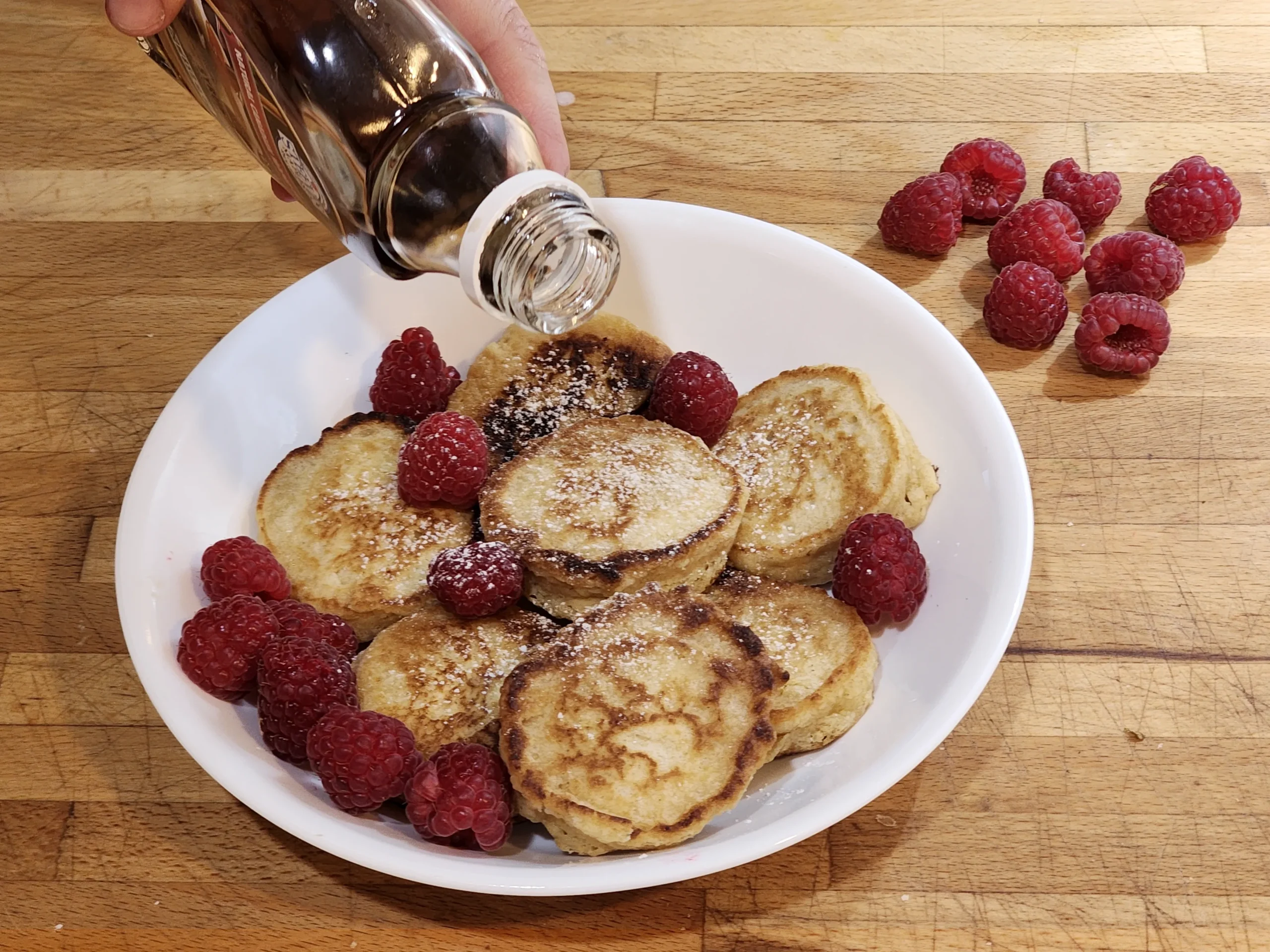 Whole wheat flour mini pancakes with maple syrup and raspberries.