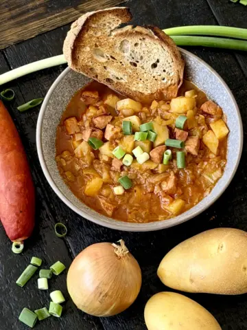 Potato goulash with sausage served in a bowl with bread