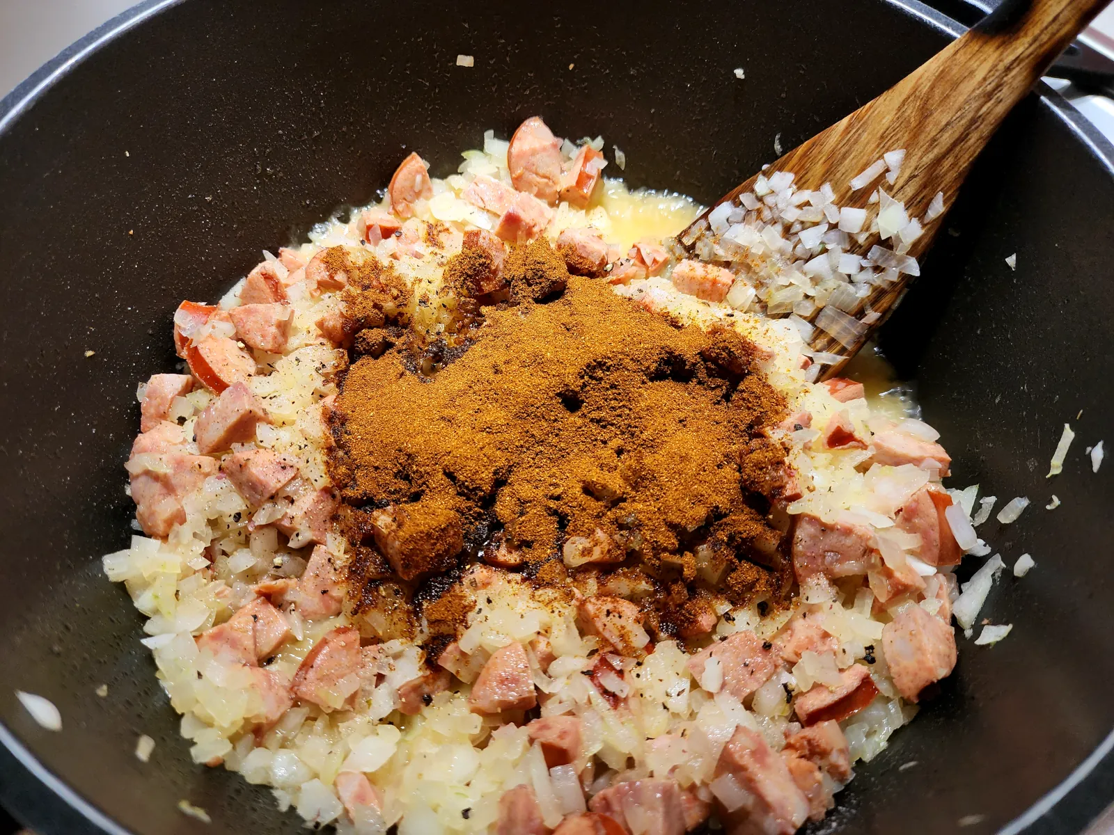 Adding spices to the pot of goulash with onion and sausages
