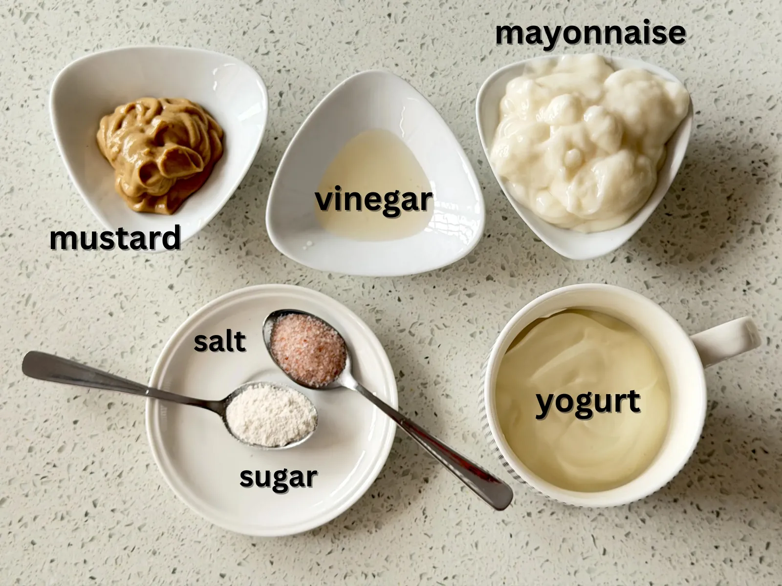 Condiments and spices for potato salad - mustard, vinegar, mayonnaise, yogurt, salt and sugar  - laid out in small bowls.