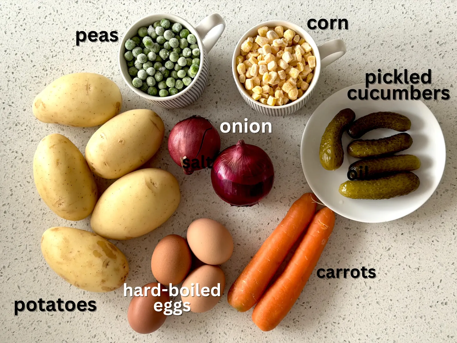Ingredients for potato salad - potatoes, onion, eggs, carrots, peas, corn and pickled cucumbers - laid out on a table.