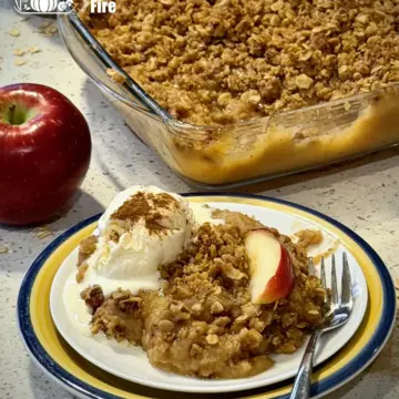 An applesauce crisp served with ice cream on a plate, with full baking tray of applesauce crisp in the background