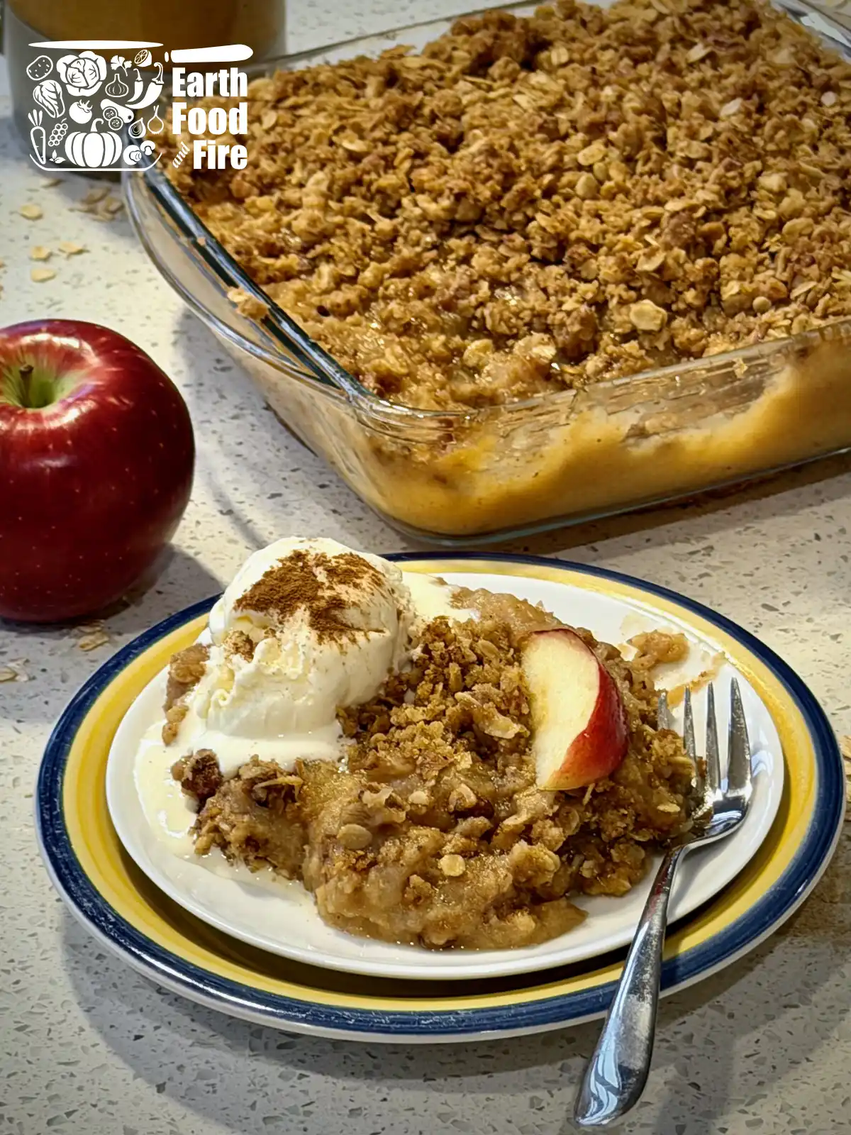 An applesauce crisp served with ice cream on a plate, with full baking tray of applesauce crisp in the background
