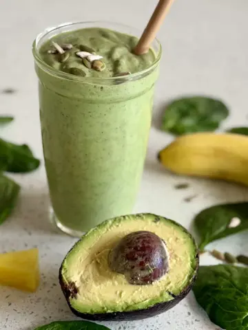 Avocado smoothie with pieces of pineapple, whole banana, half of the avocado, spinach leaves and seeds