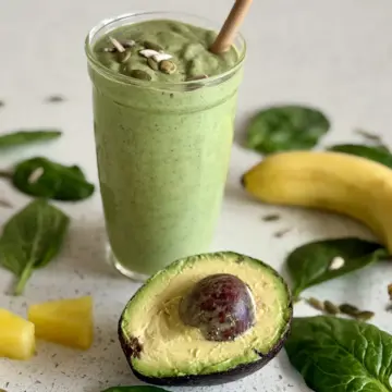 Avocado smoothie with pieces of pineapple, whole banana, half of the avocado, spinach leaves and seeds