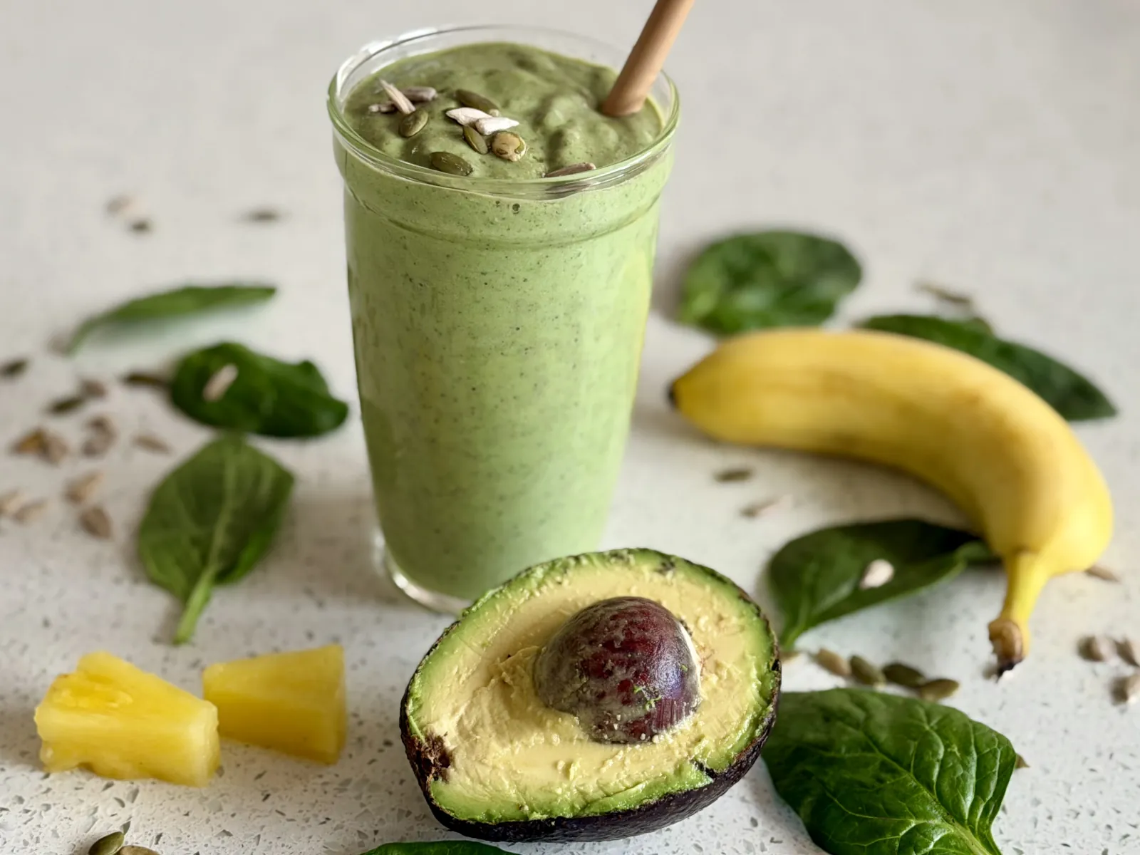 Avocado smoothie with pieces of pineapple, whole banana, half of the avocado, spinach leaves and seeds
