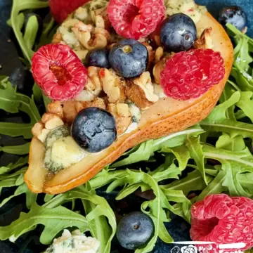 Baked pears recipe with melted blue cheese, toasted walnuts, fresh blueberries and raspberries on a bed of arugula, drizzled with honey