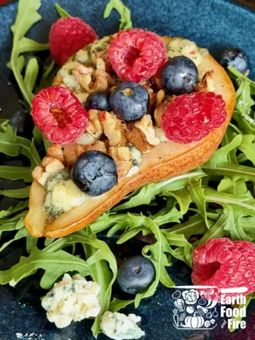 Baked pears recipe with melted blue cheese, toasted walnuts, fresh blueberries and raspberries on a bed of arugula, drizzled with honey