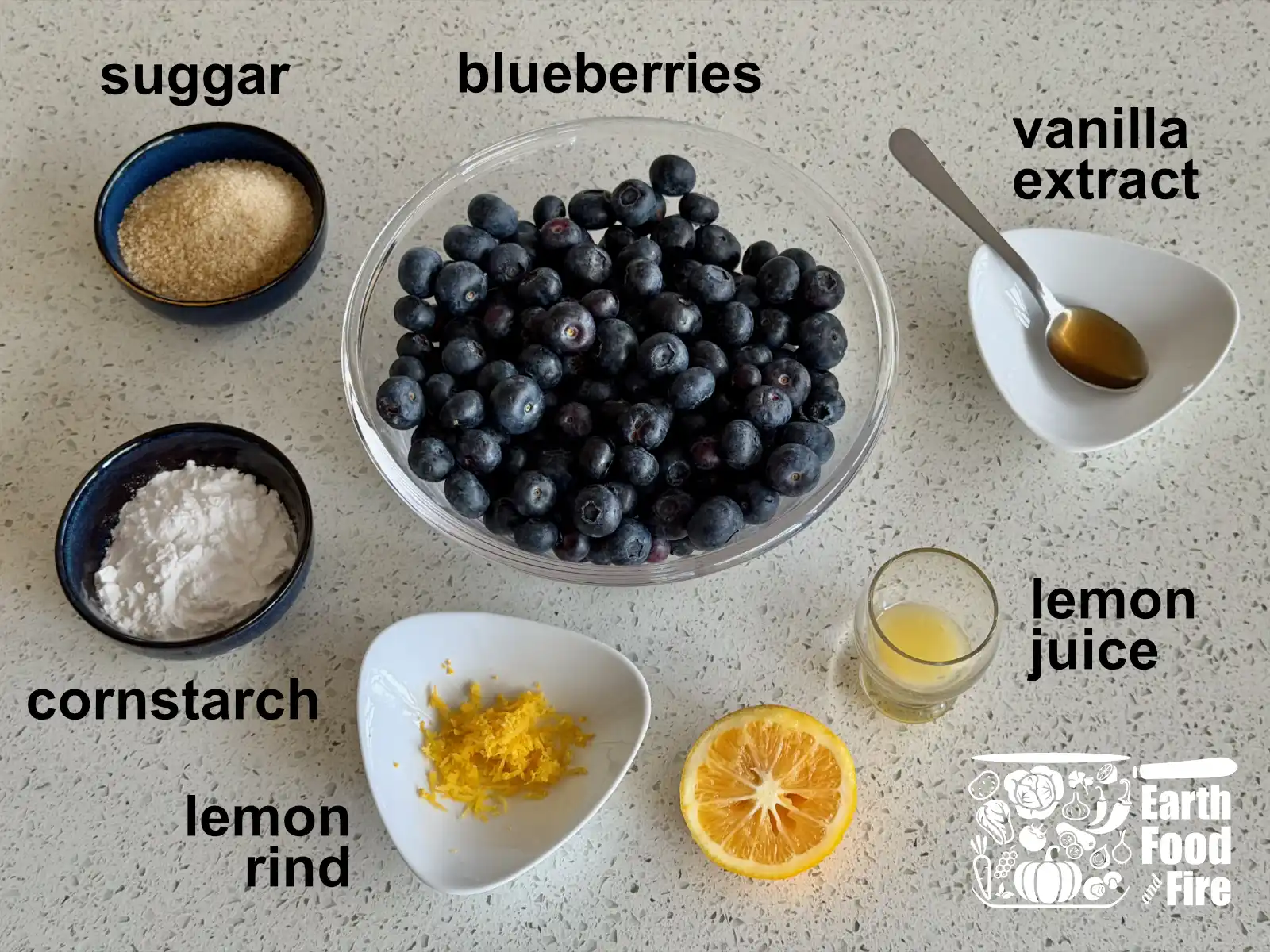 Ingredients for the blueberry crumble recipe filling laid out on table - blueberries, sugar, vanilla extract, cornstarch, lemon rind and lemon juice