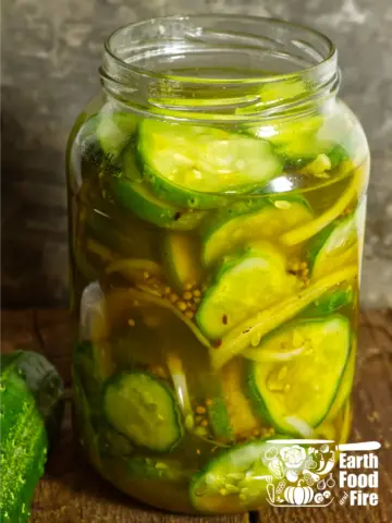 A glass jar of homemade bread and butter refrigerator pickles with sliced onion and mustard seed visible in the brine
